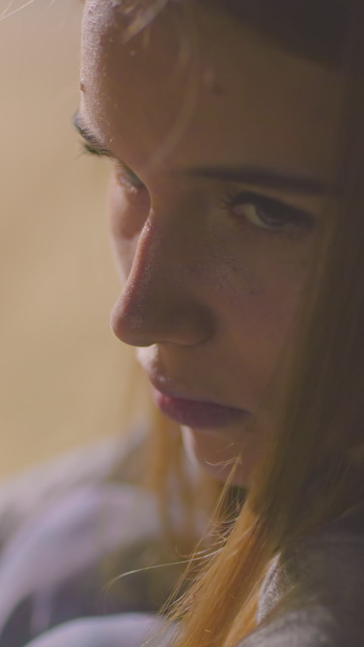 Close-up of tired young woman lifting her head slowly, showing signs of exhaustion and deep thought, surrounded by soft blurred background with warm tones of an evening park setting