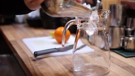 barista preparing a pitcher of lemonade by pouring ice into a pitcher at a restaurant bar