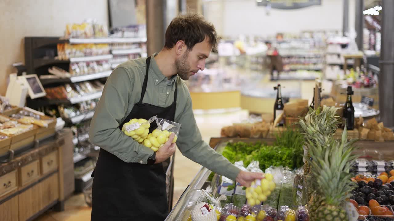 trabajador de una tienda de comestibles hombre barbudo caucásico arreglando patatas empaquetadas en un delantal en una tienda de comestibles de supermercado orgánico moderno