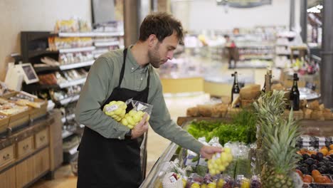 Grocery-store-worker-caucasian-bearded-guy-arranging-packed-potato-in-apron-at-modern-organic-supermarket-grocery-store