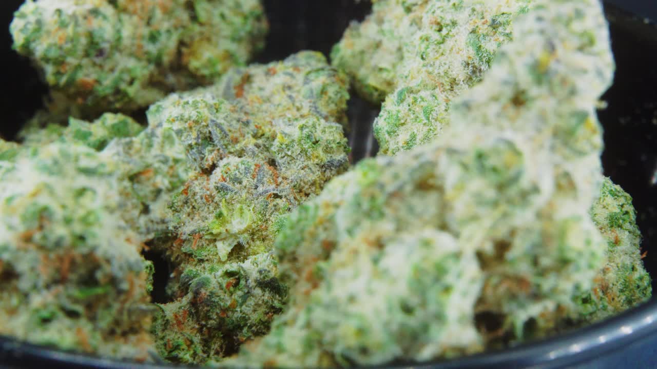 Macro Green Dried Marijuana Buds Close Up concept Shot, pile of dried marijuana plants, orange trichomes strains, in small black shiny bawl, on a rotating stand, studio lights, slow motion, 4K video