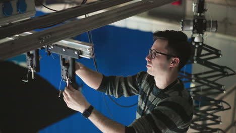 technician adjusting overhead lighting control unit in studio, focusing on precise positioning and securing equipment, ensuring rigging system is stable and properly aligned for filming or production
