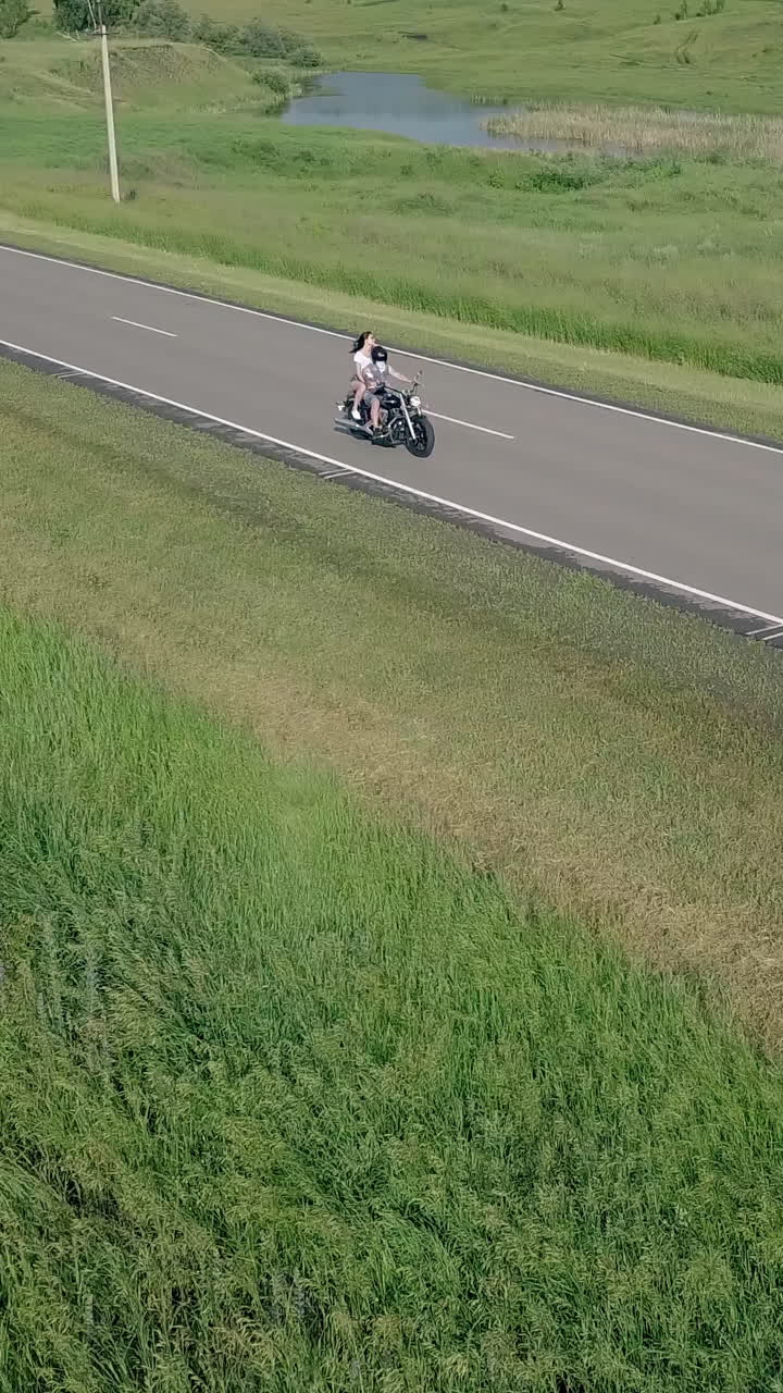 inspiring aerial view couple on black modern motorcycle drives along road between green fields with lake