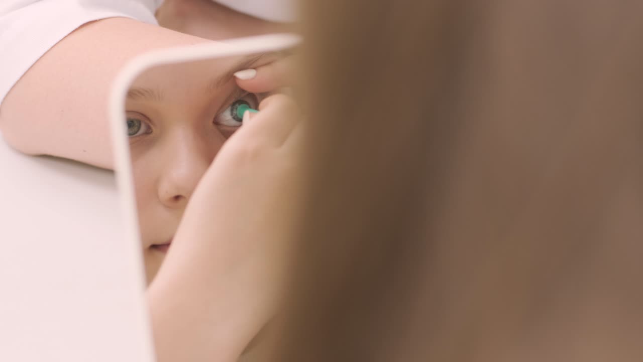 어린 소녀는 의사와 함께 거울 앞에 콘택트 렌즈를 놓습니다. 콘택트렌즈를 입합니다.