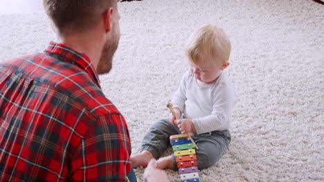 dad playing ukulele to toddler son, over shoulder view