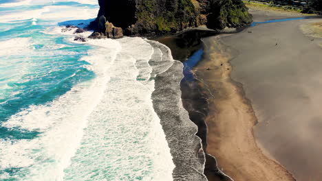 Waves-crashing-to-black-sand-Piha-Beach,-Lion-Rock-and-New-Zealand-coastal-reveal