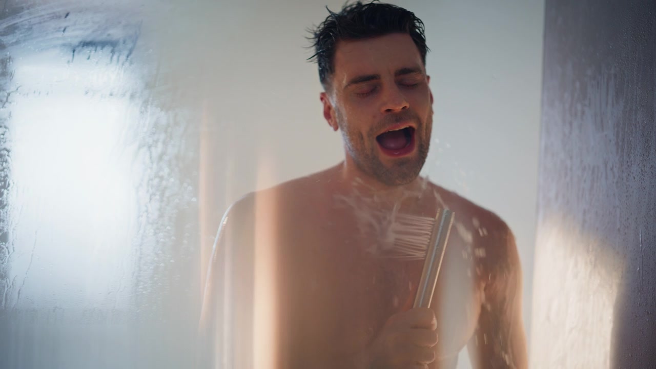 Man singing in shower holding showerhead like microphone. Happy guy bathing
