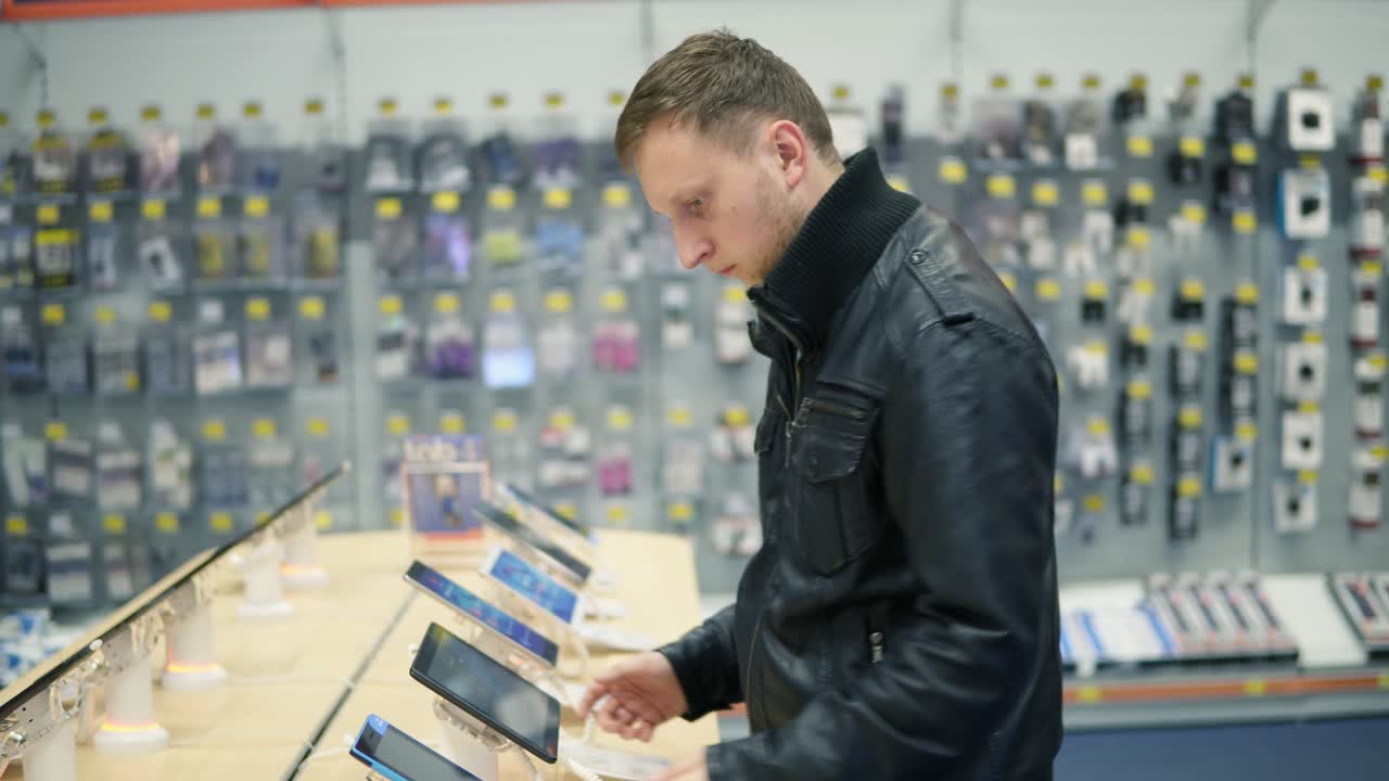 joven cliente masculino eligiendo una nueva tableta en una tienda, comprobando cómo funciona
