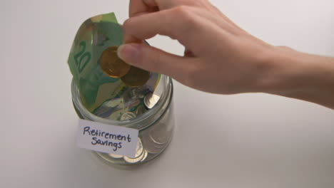 a caucasian woman's hand puts two loonies into a &quot;retirement savings&quot; jar