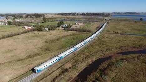 long passenger train traveling through countryside, blue and white cars, near buenos aires