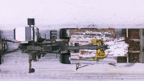 grapple log loader on snowy terrain places bunch of logs on truck