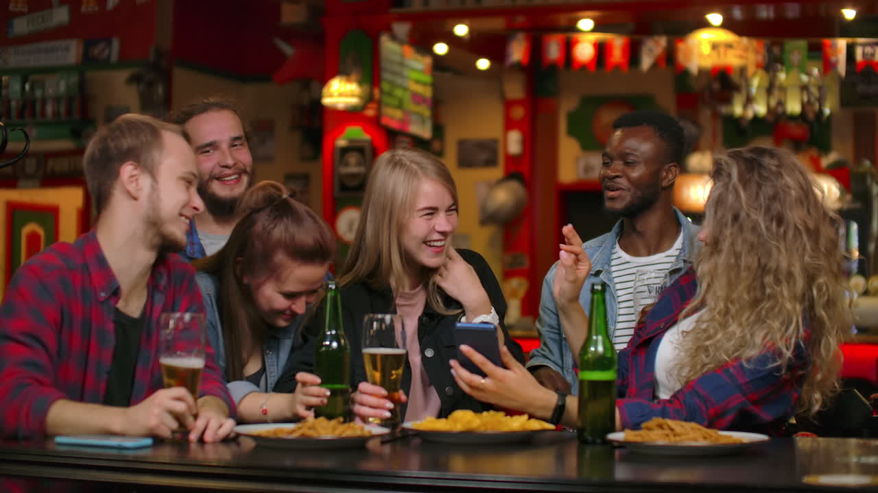 A large group of friends in the bar sitting at the table laughing and chatting drinking beer.
