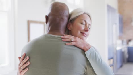 Mixed-race-senior-couple-hugging-each-other-at-home