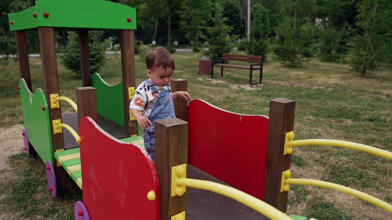 Caucasian toddler boy runs by the wooden bridge on the playground. Little boy spending time outdoors in summer.