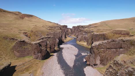 Winding-river-through-a-dramatic-canyon-landscape-under-clear-skies,-highlighting-green-grass-and-serene-nature,-shot-from-an-aerial-perspective-in-Iceland