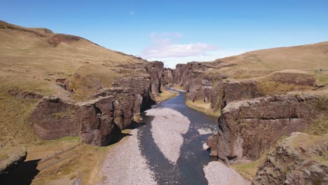 un río sinuoso a través de un espectacular paisaje de cañón bajo un cielo despejado, destacando la hierba verde y la naturaleza serena, tomada desde una perspectiva aérea en islandia
