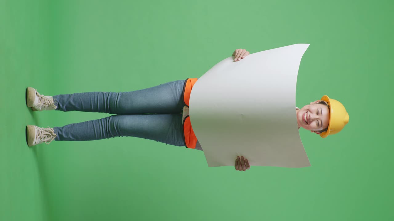 cuerpo lleno de ingeniera femenina asiática con casco de seguridad mirando el plano en sus manos mientras estaba de pie en el estudio de fondo de la pantalla verde