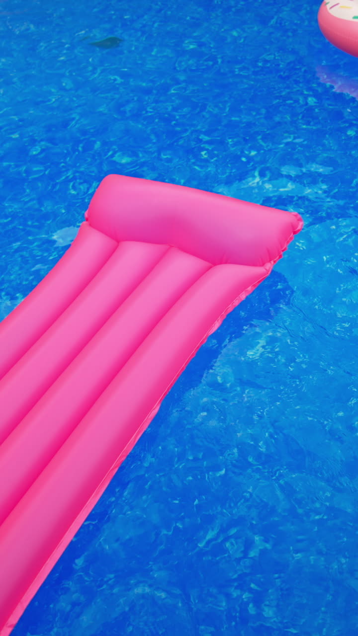 Swimming circle and inflatable mattress on the water surface. Swimming appliances in the pool with no people in. View from top. Vertical video