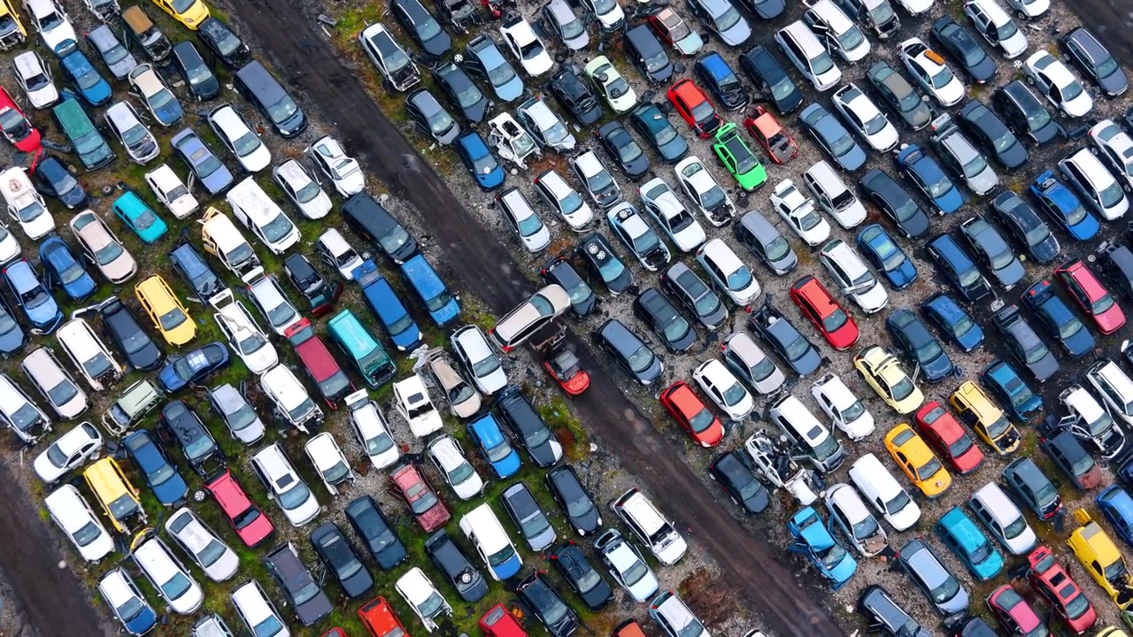 Vista dall'alto di auto rottamate con carrello elevatore in funzione. Inquadratura dall'alto di veicoli colorati in un centro di riciclaggio con un carrello elevatore che sposta una scocca d'auto