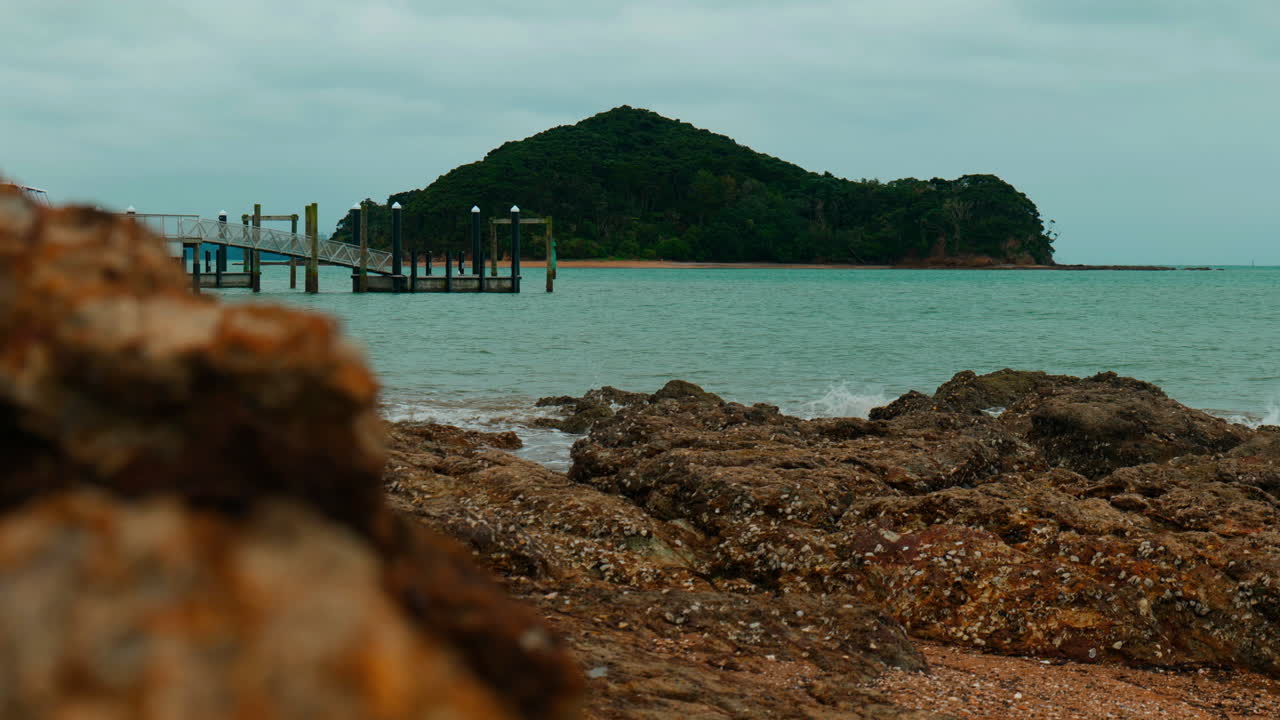 Slow-motion mid shot of Island with pier in front at Piahia, New Zealand