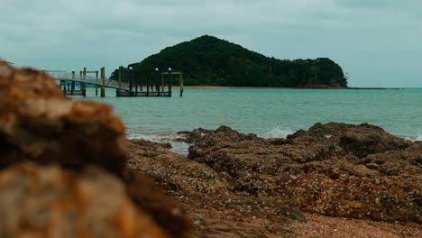 Slow-motion-mid-shot-of-Island-with-pier-in-front-at-Piahia,-New-Zealand