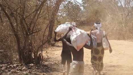 african village people carrying goods along dirt road on their heads. wide shot along road.
