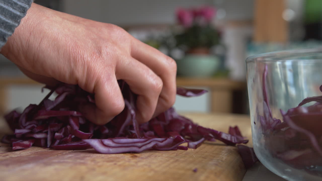 cerrar la mano de una mujer cortando cebollas rojas italianas con un cuchillo afilado redondeado en una tabla de madera en su cocina, luego llenando lentamente la fiambrera de vidrio