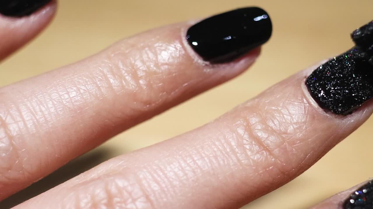 Detailed view of applying glitter over black nail polish on fingernails.