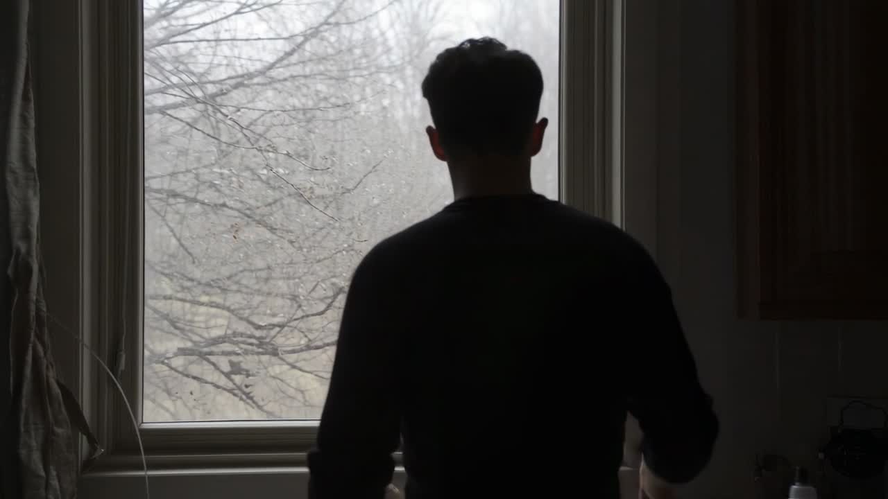 Turning man dark-shirted moving to sink misty light drawing using faucet and watching window trees