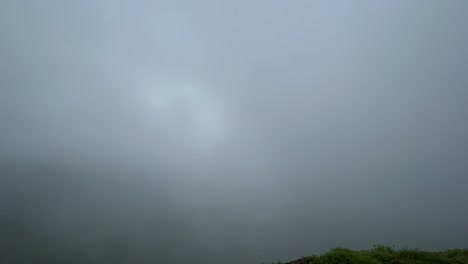 a steady wide timelapse shot of clouds passing by, covering civilisation of houses and roads downhill, taken from the top of a mountain