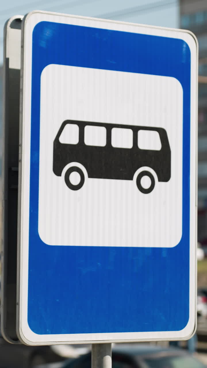 vista cercana de un letrero de parada de autobús de la ciudad en un día soleado con una carretera ocupada y edificios en el fondo
