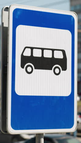 close view of a city bus stop sign on a sunny day with a busy road and buildings in the background