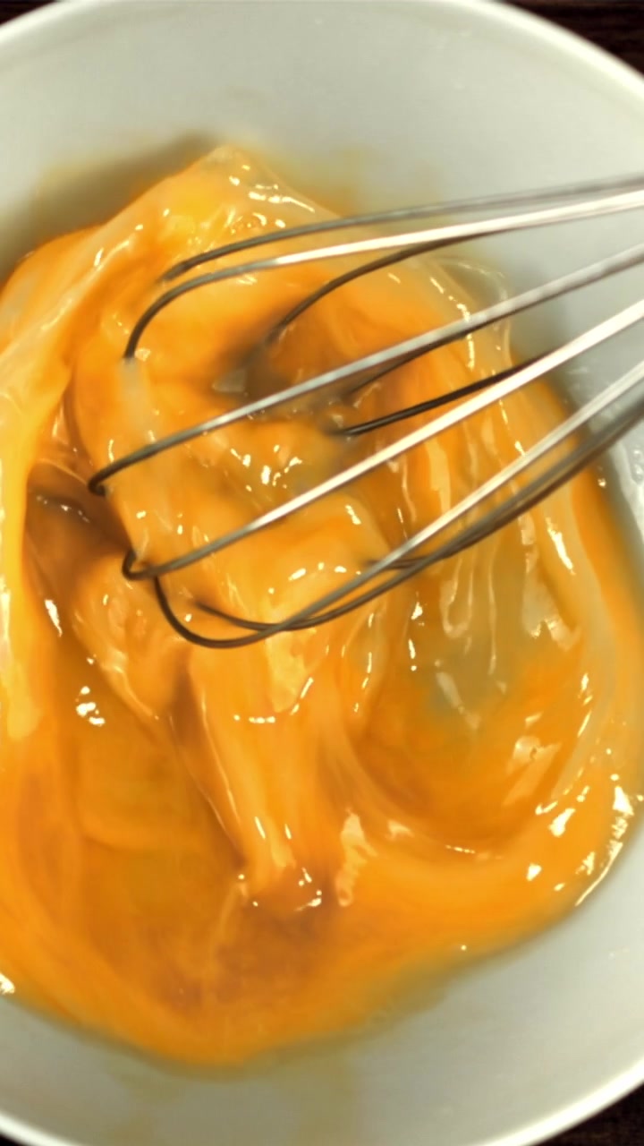 Primer plano de huevos crudos batiéndose en un cuenco blanco.