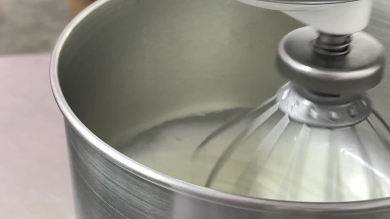 Commercial kitchen shot of electric mixer beating and mixing and whipping egg white, preparing for perfect swiss meringue buttercream.
