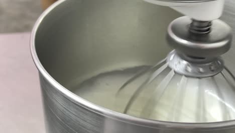 commercial kitchen shot of electric mixer beating and mixing and whipping egg white, preparing for perfect swiss meringue buttercream.