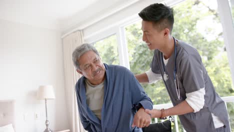 diverse male doctor helping senior male patient standing up at home, slow motion