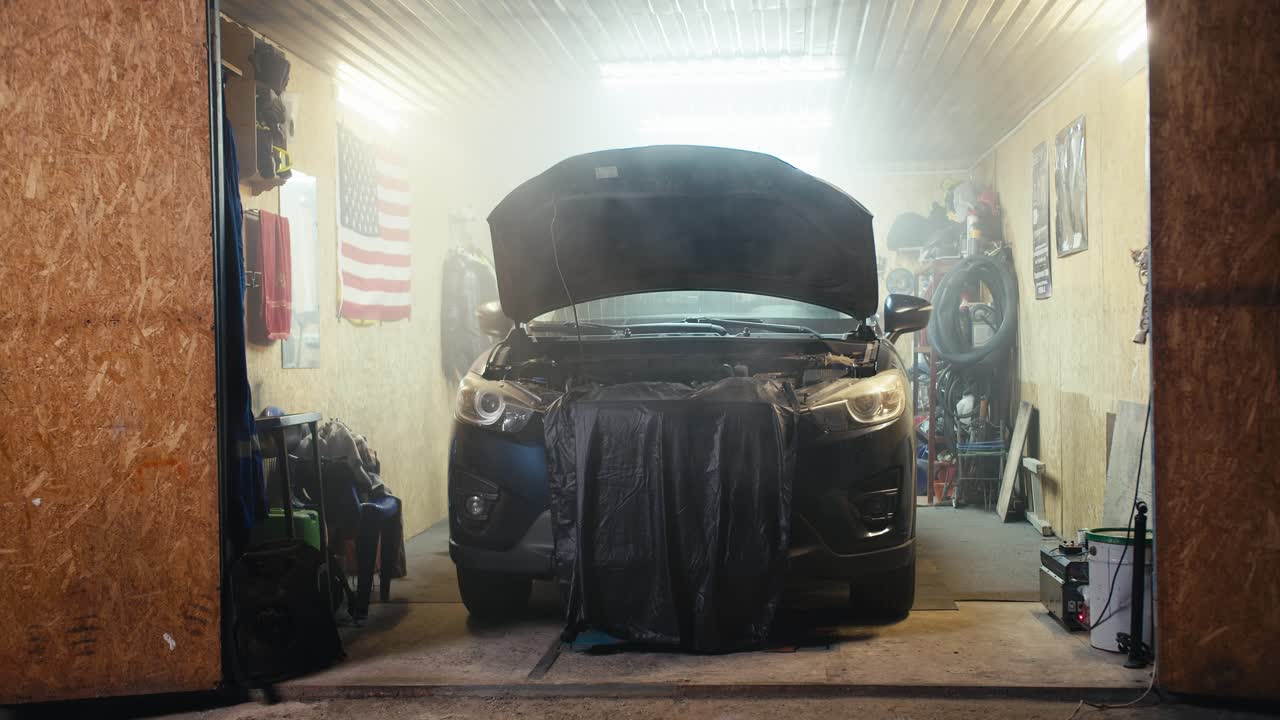 워크 차고에 주차되어 있으며 약간의 안개로 여있는 자동차의 리뷰: 작업 중 휴식과 자동차의 후드의 수리 중에 은 회색 천을 사용하여 자동차의 후드가 아집니다.