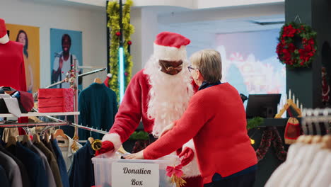 Retail-assistant-dressed-as-Santa-Claus-collecting-unneeded-clothes-from-clients-in-donation-box,-giving-them-as-present-to-those-in-need-during-Christmas-season,-spreading-holiday-cheer