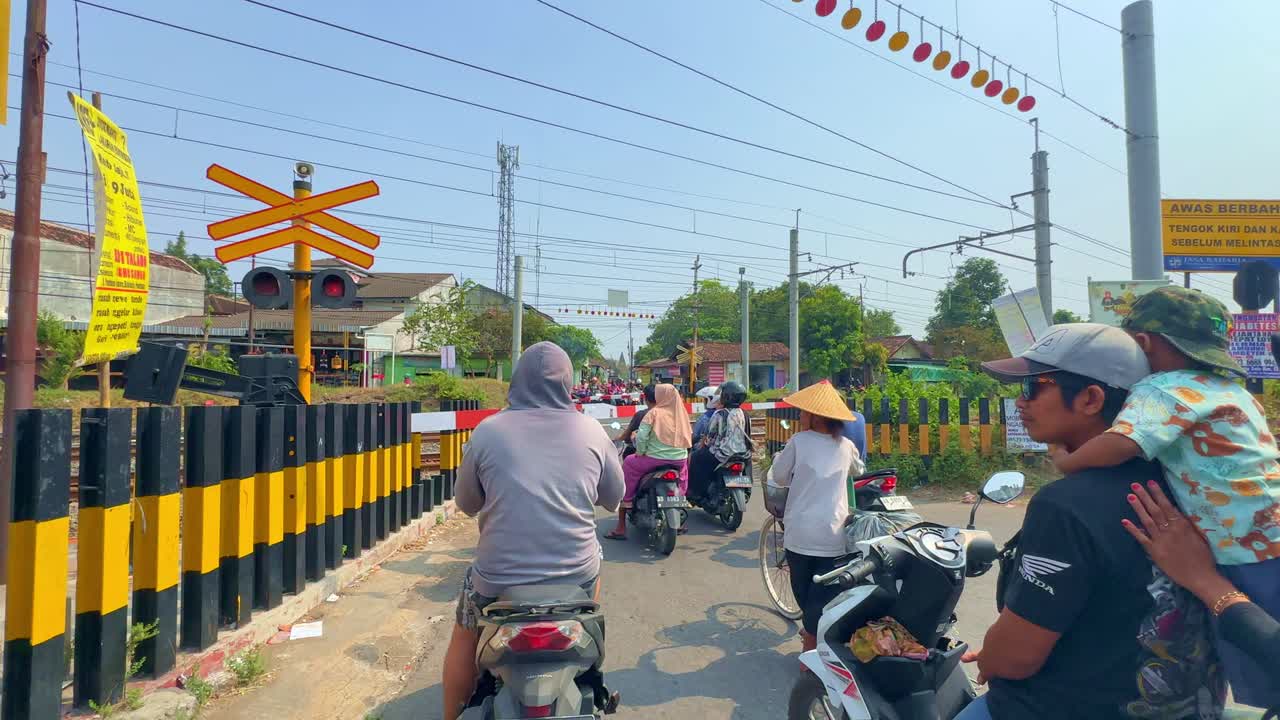 People ride motorcycle are stopped in front of the railway crossing. Waiting for the train to pass. Indonesia.