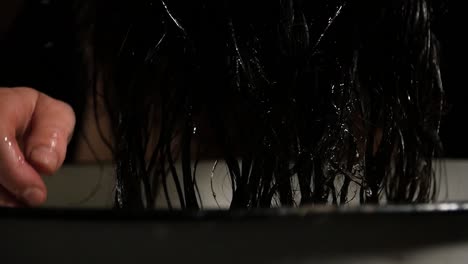 hands of young woman pouring water on her black hair in a white metal barrel at home