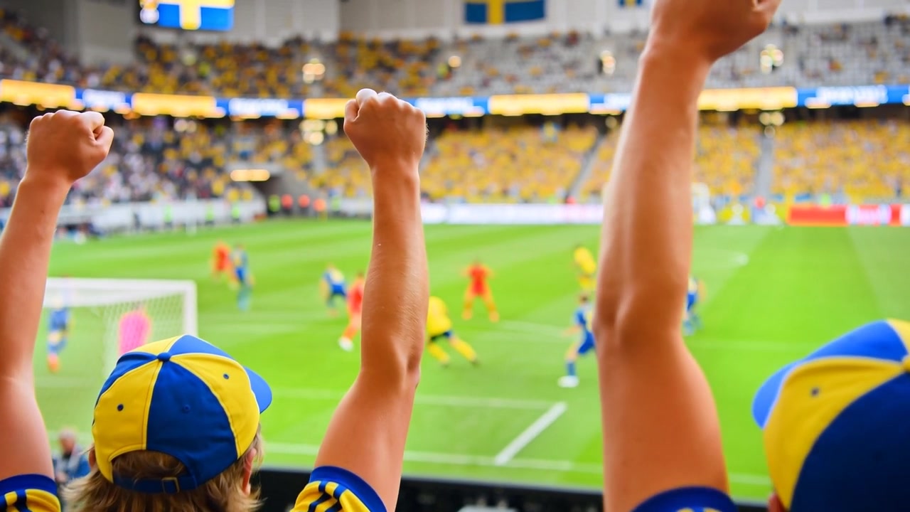Levantando los brazos, dos aficionados con equipación amarillo-azul en el estadio, apretando los puños, reaccionando a un tiro a puerta.