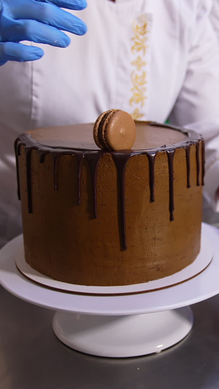 Big beautiful chocolate cake decoration in the confectionary. Pastry cook puts the macaroons on cake top. Close up. Vertical video