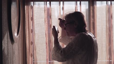 senior woman applying makeup by window