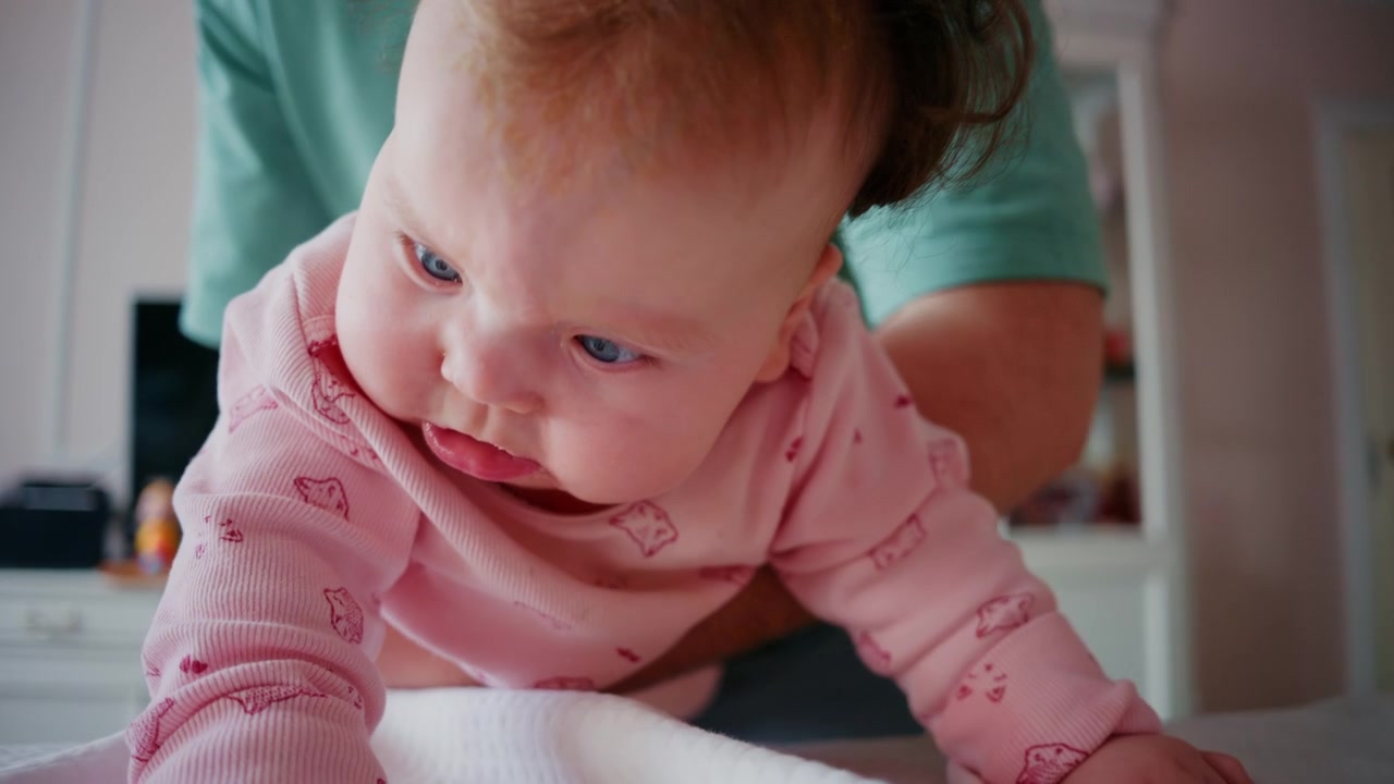 Close up of a baby being gently supported during tummy time on a padded table