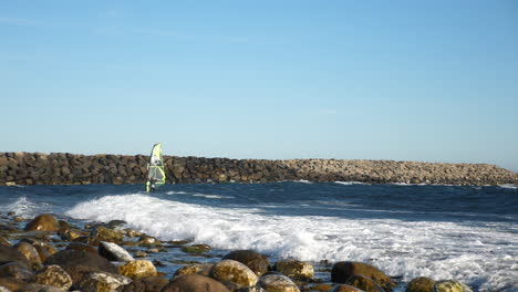 Toma-Panorámica-De-Un-Windsurfista-Noruego,-Surfeando-Una-Ola-Cerca-De-La-Costa-Rocosa,-En-El-Mar-Del-Norte,-En-El-Océano-Atlántico,-En-Un-Día-Soleado-De-Verano,-En-Lista,-Sur-De-Noruega