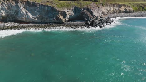 volando sobre las olas de color turquesa hacia los acantilados escarpados y la playa rocosa