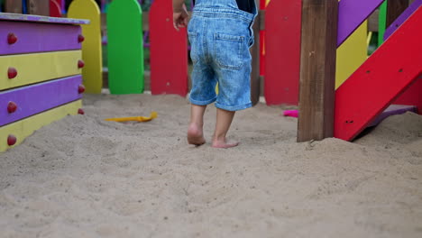 lower part of a baby boy stepping by the sand on the playground. little toddler feet come up to the colorful stairs.