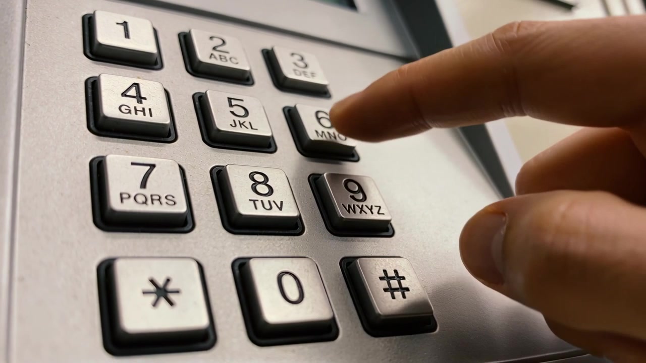 Tapping right-hand index finger contacting lower-right key, entering digits on office desk keypad