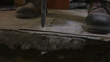 medium close up on drill bit penetrating basement concrete floor creating dust and smoke, with hand entering frame lifting up tile