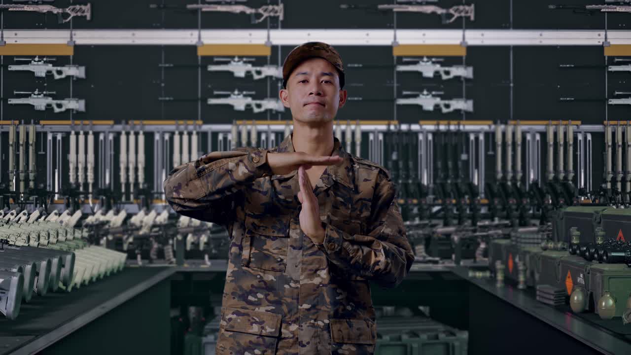 Asiatisk mandlig soldat, der kigger på kameraet og viser time out-hænder i militærvåbenhus